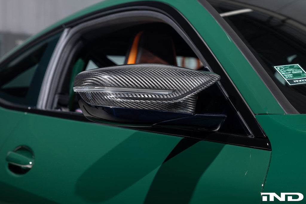 Alpha N G8X M2 M3 M4 carbon mirror cap set installed on exterior side of vehicle, showcasing sleek black carbon finish.