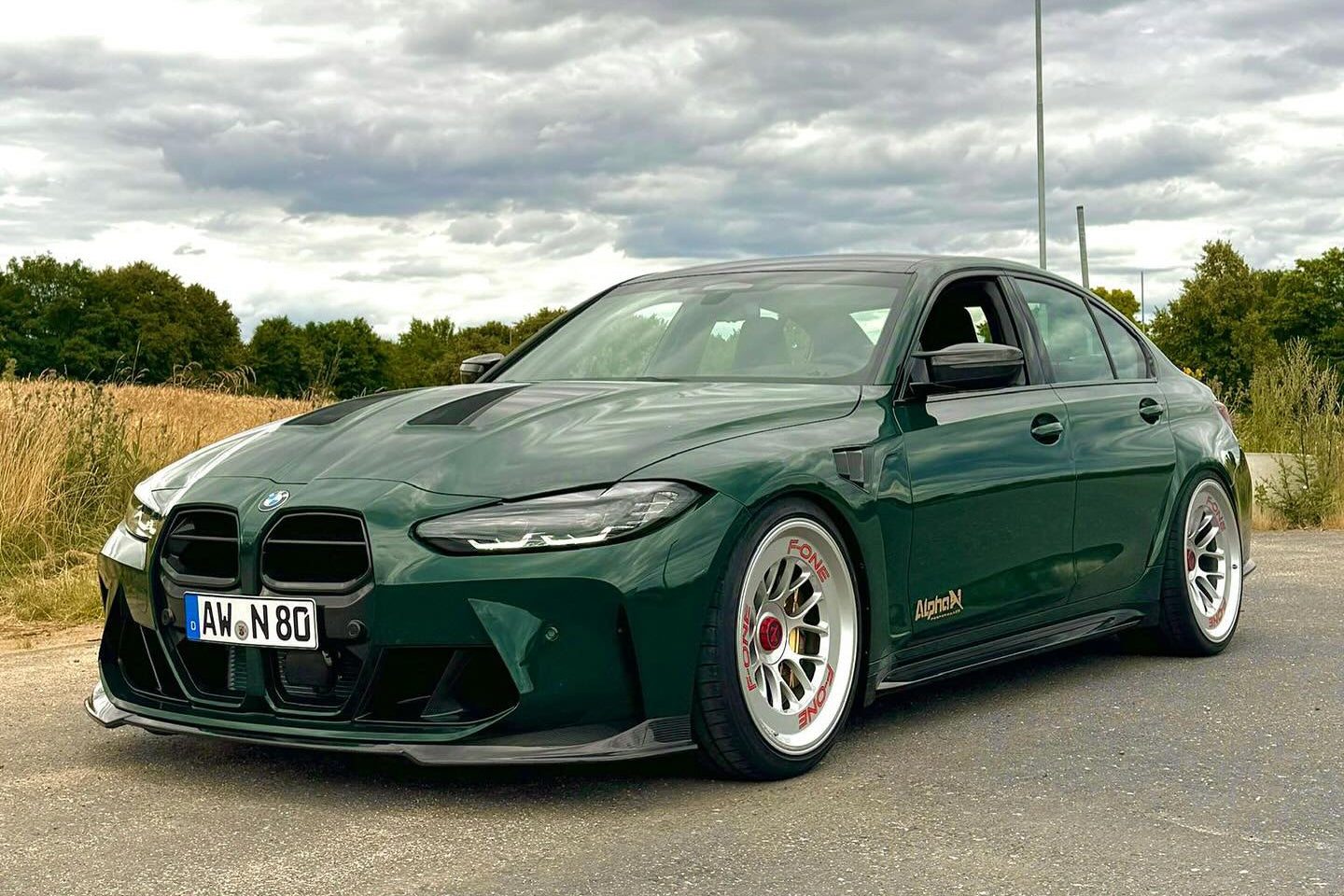 Alpha N G8X M3 M4 carbon front spoiler installed on exterior of vehicle, showcasing sleek aerodynamic design.