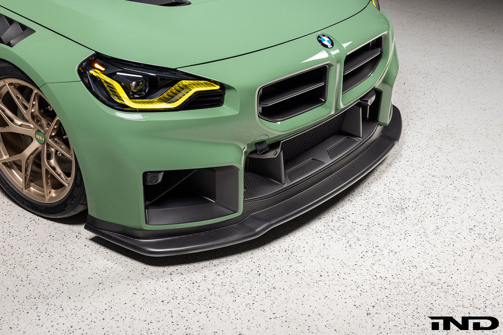 Alpha N G87 M2 Carbon Corse front splitter installed on car, matte clear finish, exterior automotive part for enhanced aerodynamics.